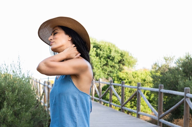 Vista lateral de la mujer posando al aire libre con sombrero y valla de madera