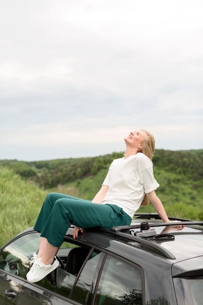 Foto gratuita vista lateral de la mujer posando encima del coche en la naturaleza