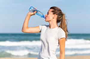 Foto gratuita vista lateral de la mujer que se mantiene hidratada durante el entrenamiento en la playa