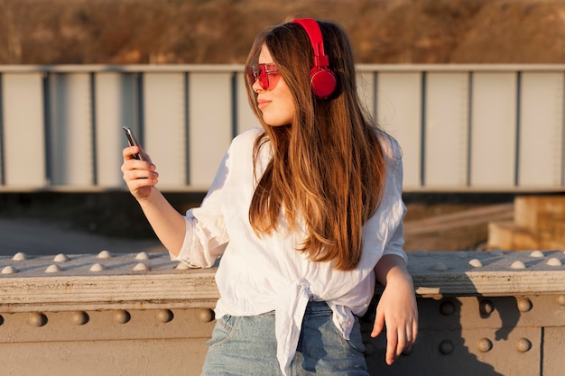 Foto gratuita vista lateral de la mujer que sostiene el teléfono inteligente mientras usa gafas de sol y auriculares