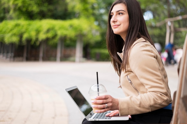 Vista lateral de la mujer que trabaja al aire libre en la computadora portátil