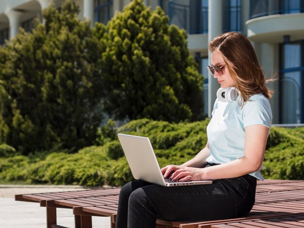 Vista lateral de la mujer que trabaja al aire libre con laptop