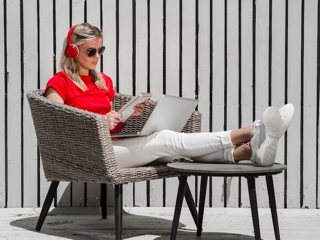 Vista lateral de la mujer que trabaja en la computadora portátil al aire libre mientras usa auriculares