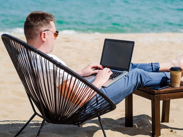 Vista lateral de la mujer que trabaja en la computadora portátil en la playa