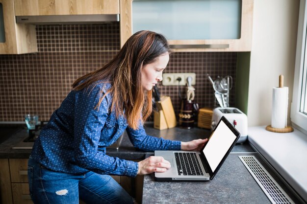 Vista lateral de una mujer que usa la computadora portátil en cocina