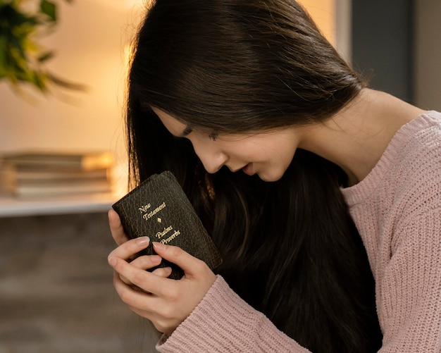 Vista lateral de la mujer rezando mientras sostiene la Biblia