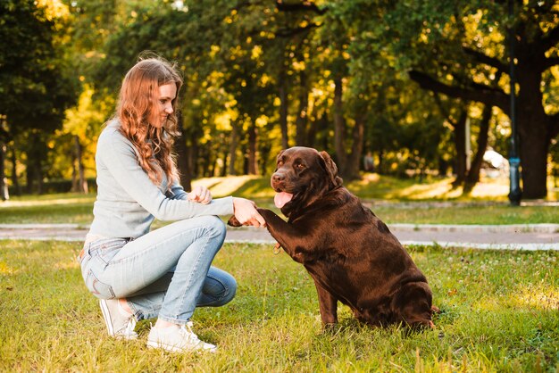 Vista lateral de una mujer sacudiendo la pata de un perro en el jardín