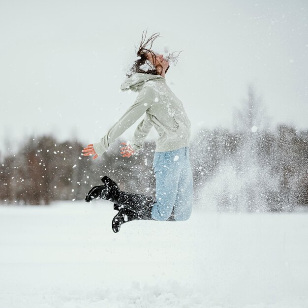 Vista lateral de la mujer saltando al aire libre en la nieve del invierno