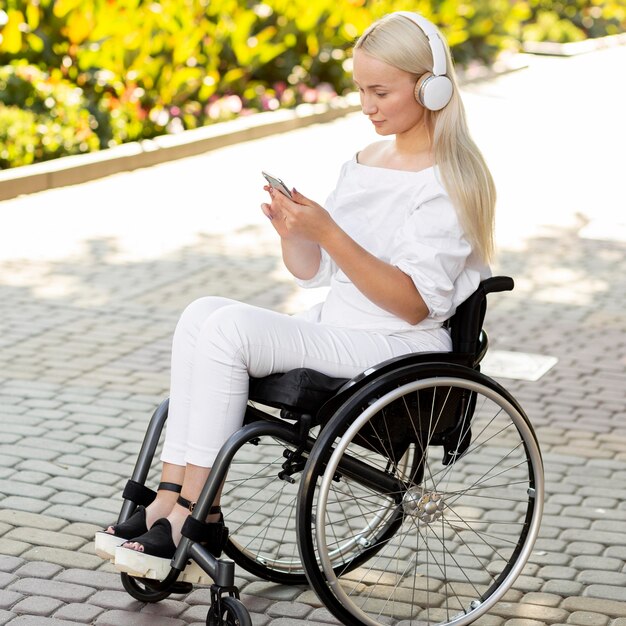 Vista lateral de la mujer en silla de ruedas con auriculares y smartphone