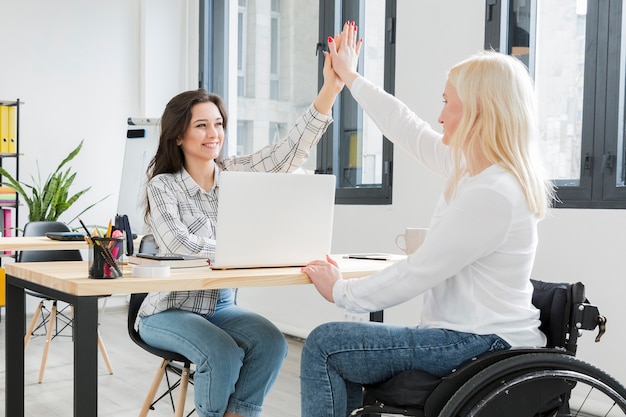 Foto gratuita vista lateral de la mujer en silla de ruedas chocando los cinco con su colega