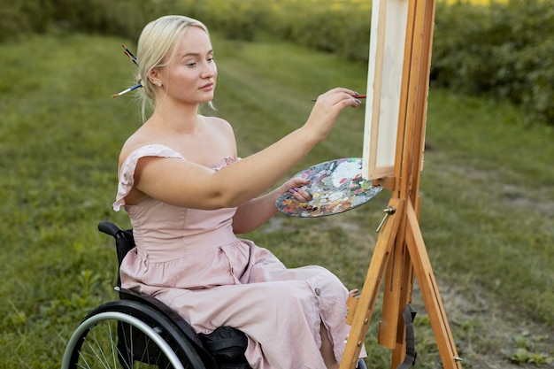 Vista lateral de la mujer en silla de ruedas pintando al aire libre