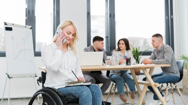 Vista lateral de la mujer en silla de ruedas trabajando desde el teléfono en la oficina