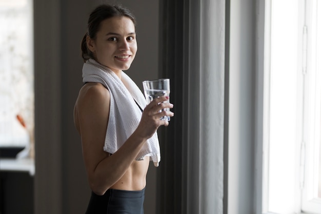 Vista lateral de la mujer sonriendo y sosteniendo un vaso de agua