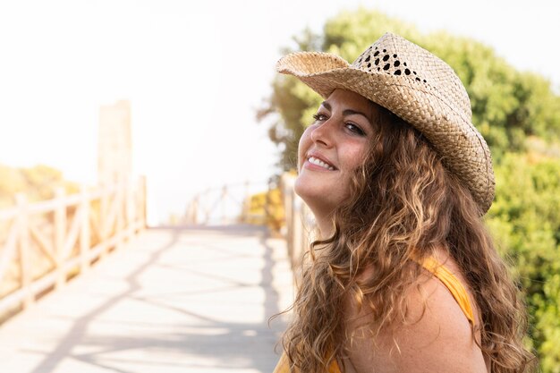 Vista lateral de la mujer sonriente en la naturaleza con sombrero