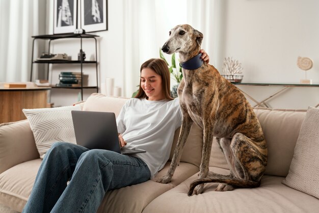 Vista lateral mujer sonriente y perro galgo en el sofá