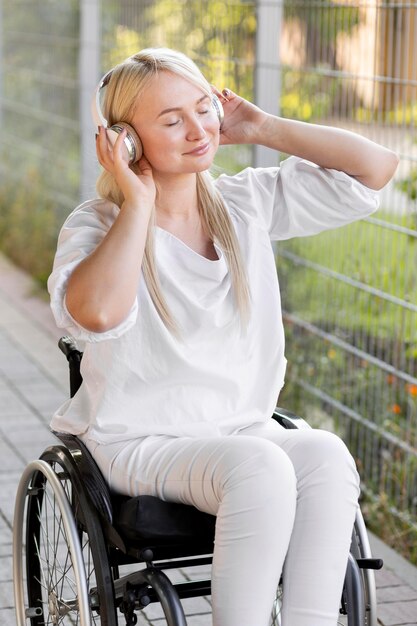 Vista lateral de la mujer sonriente en silla de ruedas con auriculares