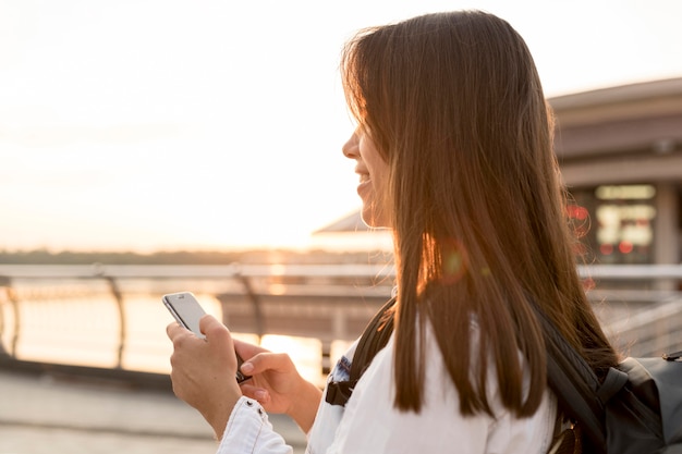 Vista lateral de la mujer sonriente con smartphone mientras viaja solo