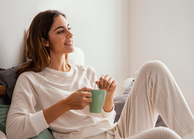 Vista lateral de la mujer sonriente tomando un café en la cama