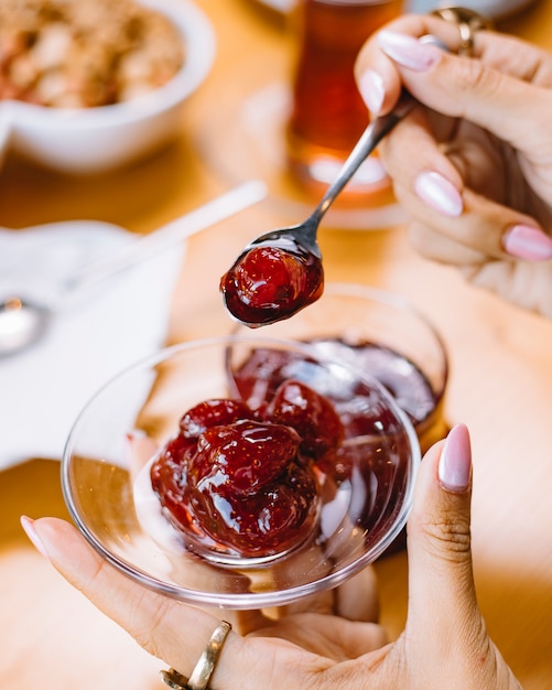 Vista lateral de una mujer sosteniendo un platillo pequeño con mermelada de fresa