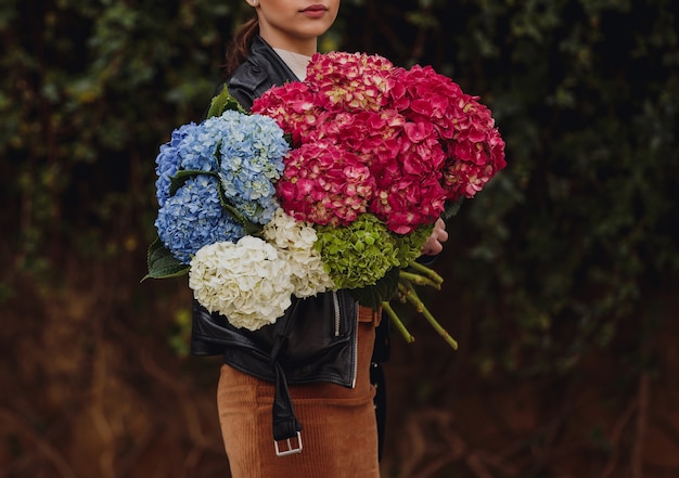 Vista lateral de una mujer sosteniendo un ramo de flores de hortensia en colores azul y blanco rosa