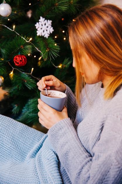 Vista lateral de mujer con taza al lado de árbol de navidad