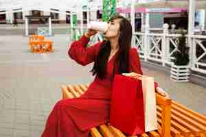 Foto gratuita vista lateral de la mujer tomando café mientras está sentado junto a bolsas de la compra.