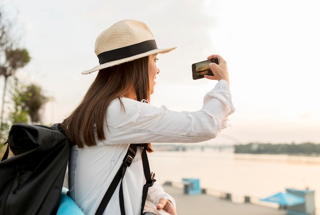 Vista lateral de la mujer tomando fotografías con el teléfono inteligente mientras viaja