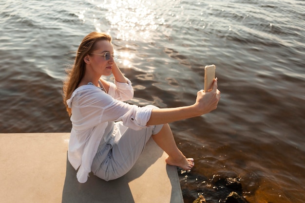 Foto gratuita vista lateral de la mujer tomando un selfie junto al lago