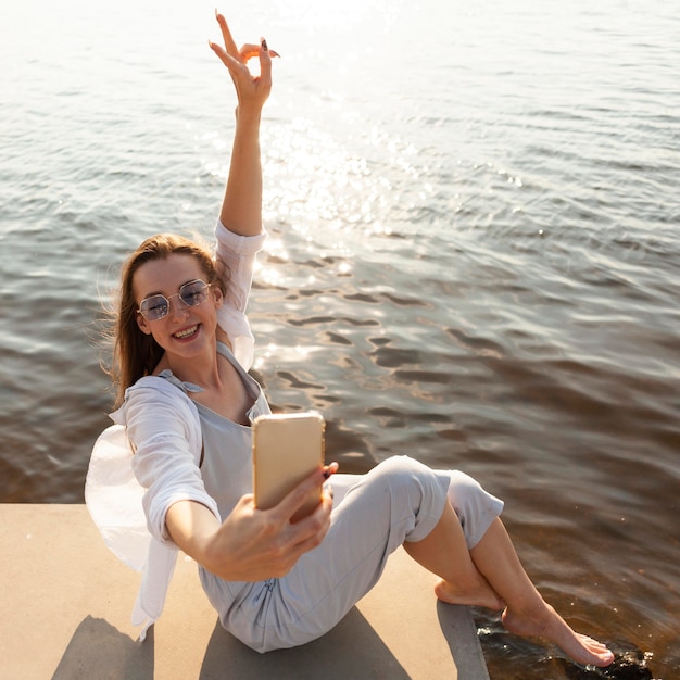 Vista lateral de la mujer tomando un selfie junto al lago