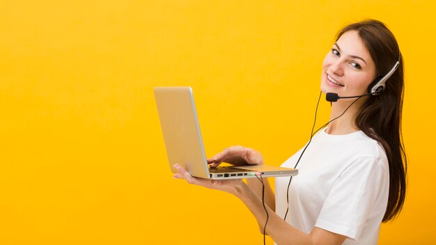 Vista lateral de la mujer usando auriculares sonriendo y sosteniendo portátil