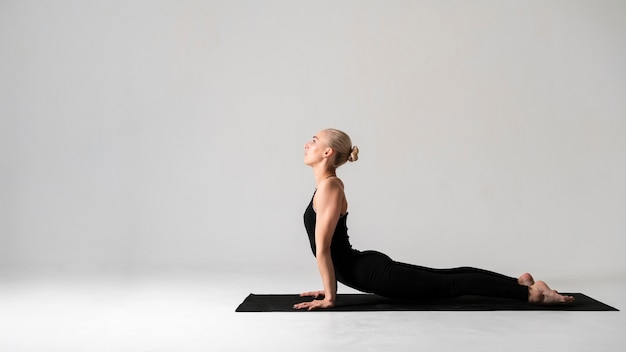 Vista lateral mujer vestida de negro con colchoneta de yoga