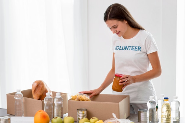 Vista lateral de la mujer voluntaria empacando alimentos en cajas para donación