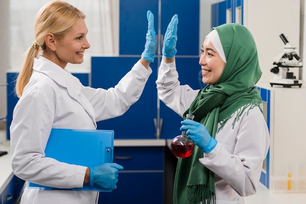 Vista lateral de mujeres científicas en el laboratorio chocando las manos