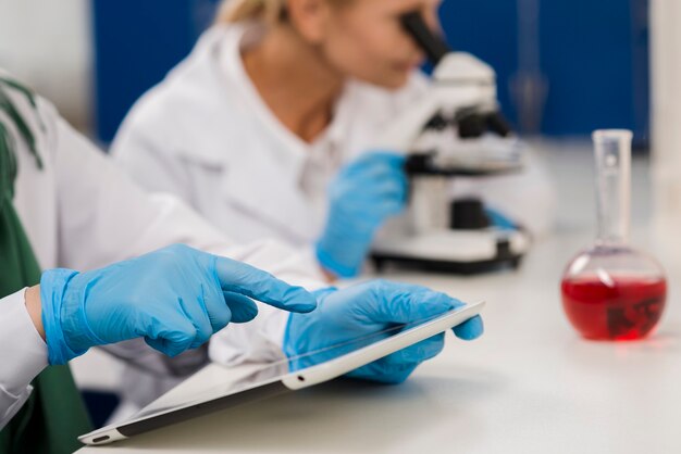 Vista lateral de mujeres científicas en el laboratorio trabajando con microscopio y tableta