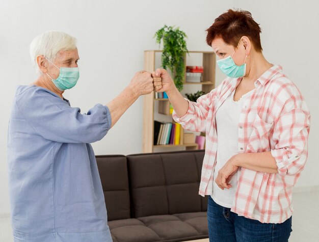 Vista lateral de mujeres mayores con máscaras médicas golpeándose los puños para saludarse