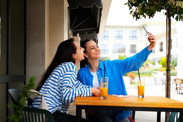 Vista lateral de mujeres sonrientes tomando selfie al aire libre