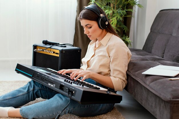 Vista lateral del músico femenino con auriculares tocando el teclado del piano