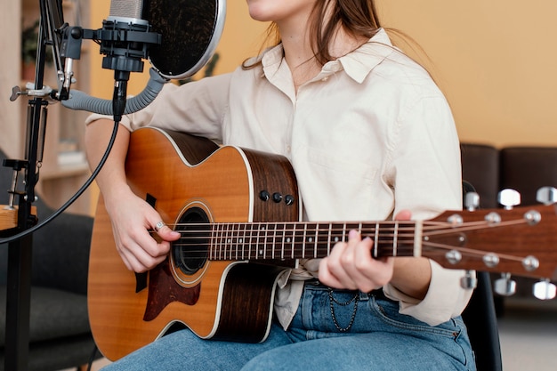 Vista lateral del músico femenino grabando canciones y tocando la guitarra acústica en casa