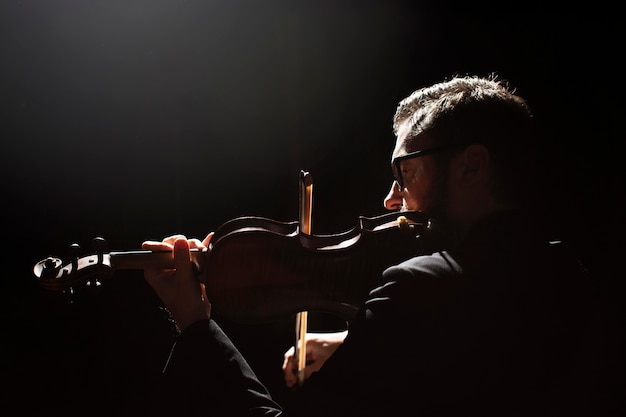 Vista lateral del músico masculino tocando el violín