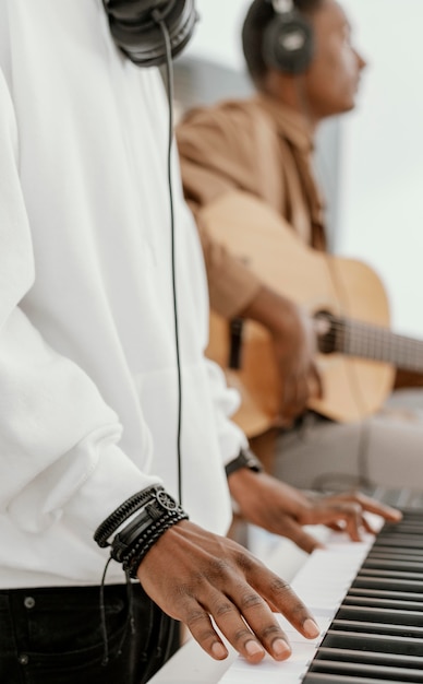 Vista lateral de los músicos masculinos en casa tocando la guitarra y el teclado eléctrico