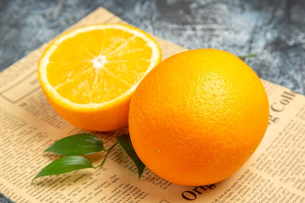 Vista lateral de la naranja cortada por la mitad y entera fresca con hojas de periódico sobre fondo gris