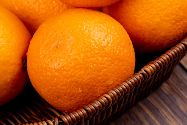 Vista lateral de naranjas frescas maduras en una cesta de mimbre sobre superficie de madera