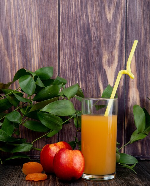 Vista lateral de nectarinas frescas maduras con un vaso de jugo de durazno en madera rústica