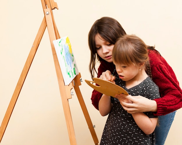 Foto gratuita vista lateral de niña ayudando a niña con pintura de síndrome de down