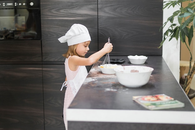 Foto gratuita vista lateral de una niña batiendo la mezcla en un tazón sobre la encimera de la cocina