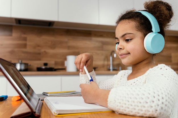 Foto gratuita vista lateral de la niña durante la escuela en línea con tableta y auriculares