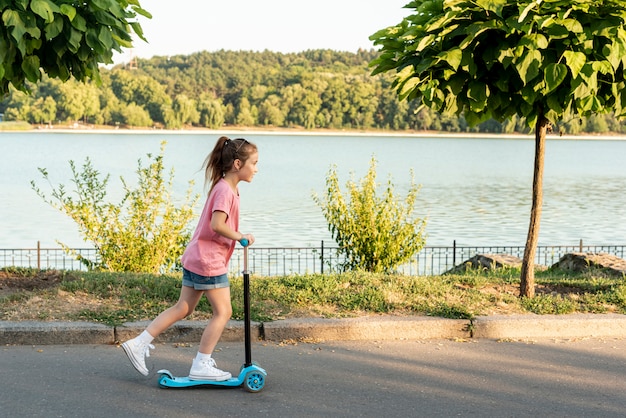 Vista lateral de la niña montando scooter azul