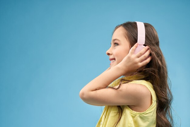 Vista lateral de una niña positiva en auriculares disfrutando de la música