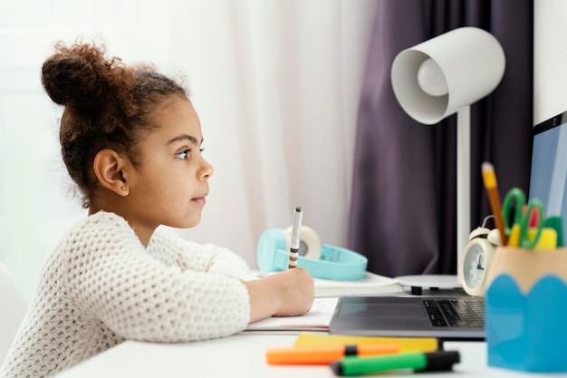 Vista lateral de la niña que asiste a la escuela en línea en casa usando laptop