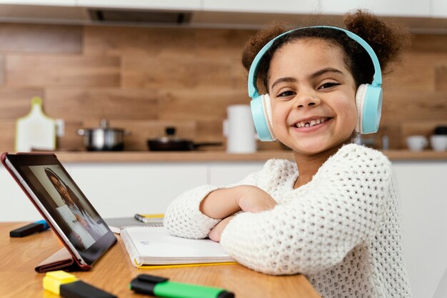 Vista lateral de la niña sonriente durante la escuela en línea con tableta y auriculares